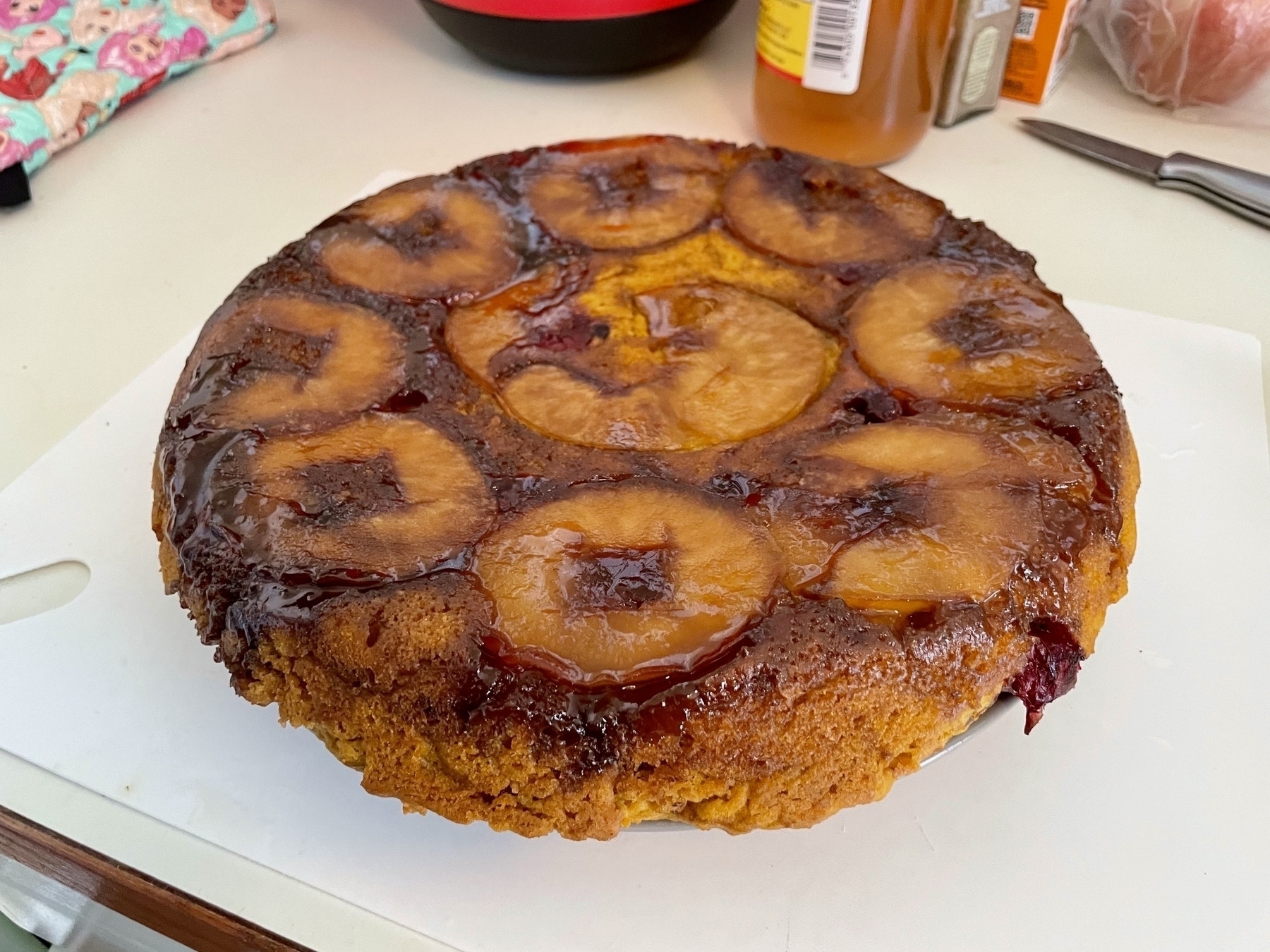 The finished cake turned out onto a plate that’s really too small of it, the crumb is orange-golden and it’s topped with the cooked apples and brown sugar butter syrup but the cranberries are basically cooked into nothingness 
