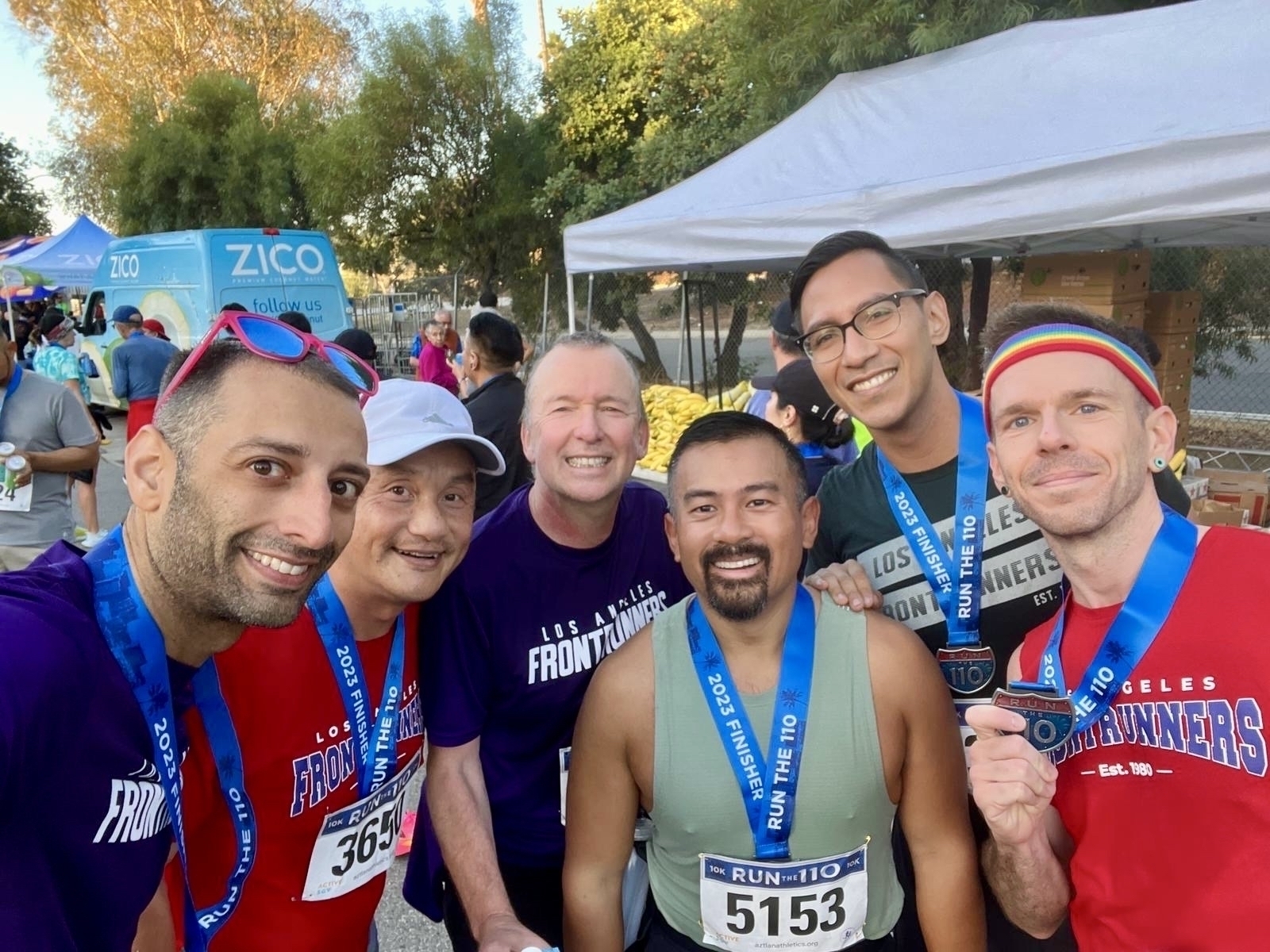 A group of men in running gear, wearing finisher medals shaped like a highway sign, pose for a photo 