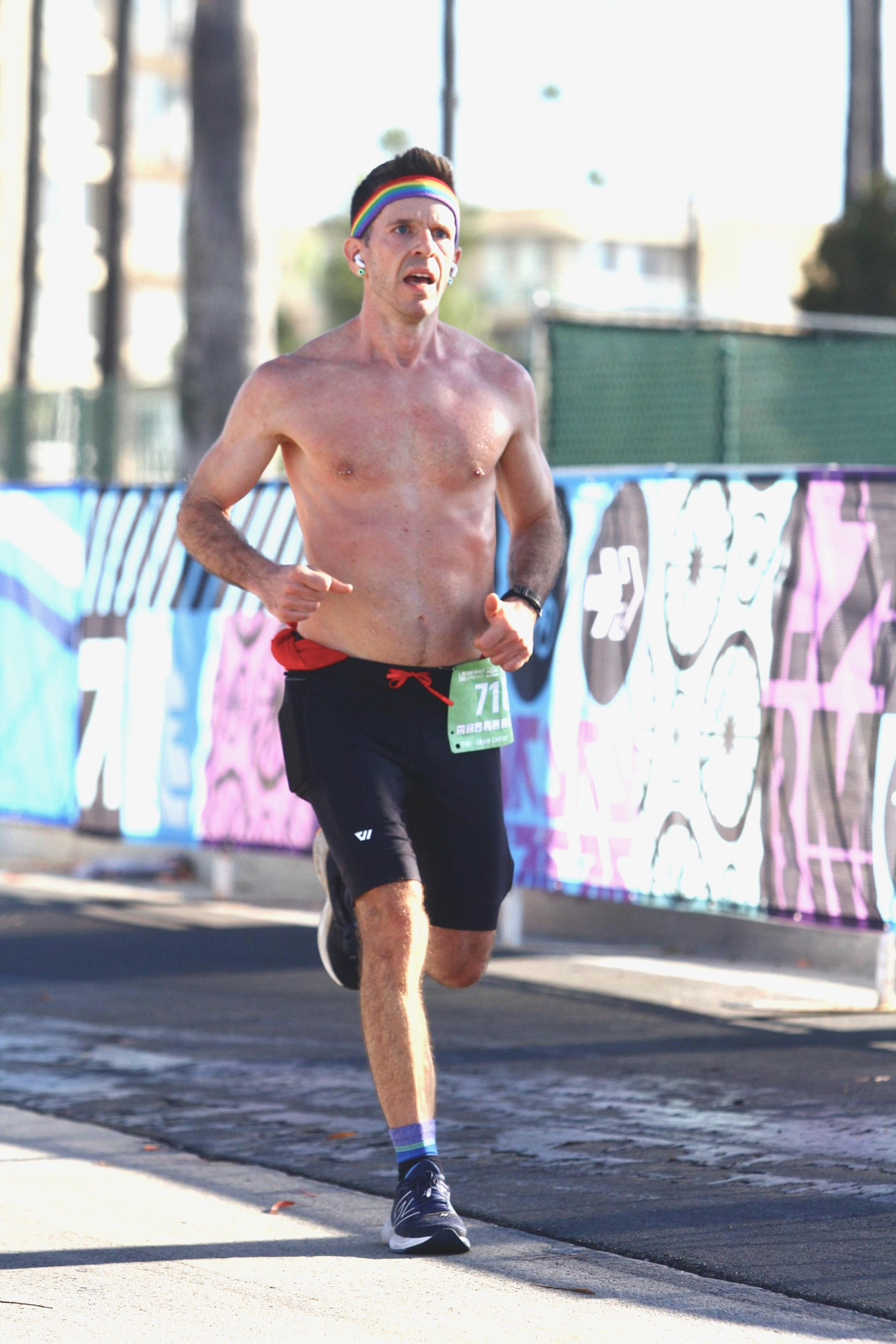 A man in short tights and a rainbow headband running down the finish chute of a race