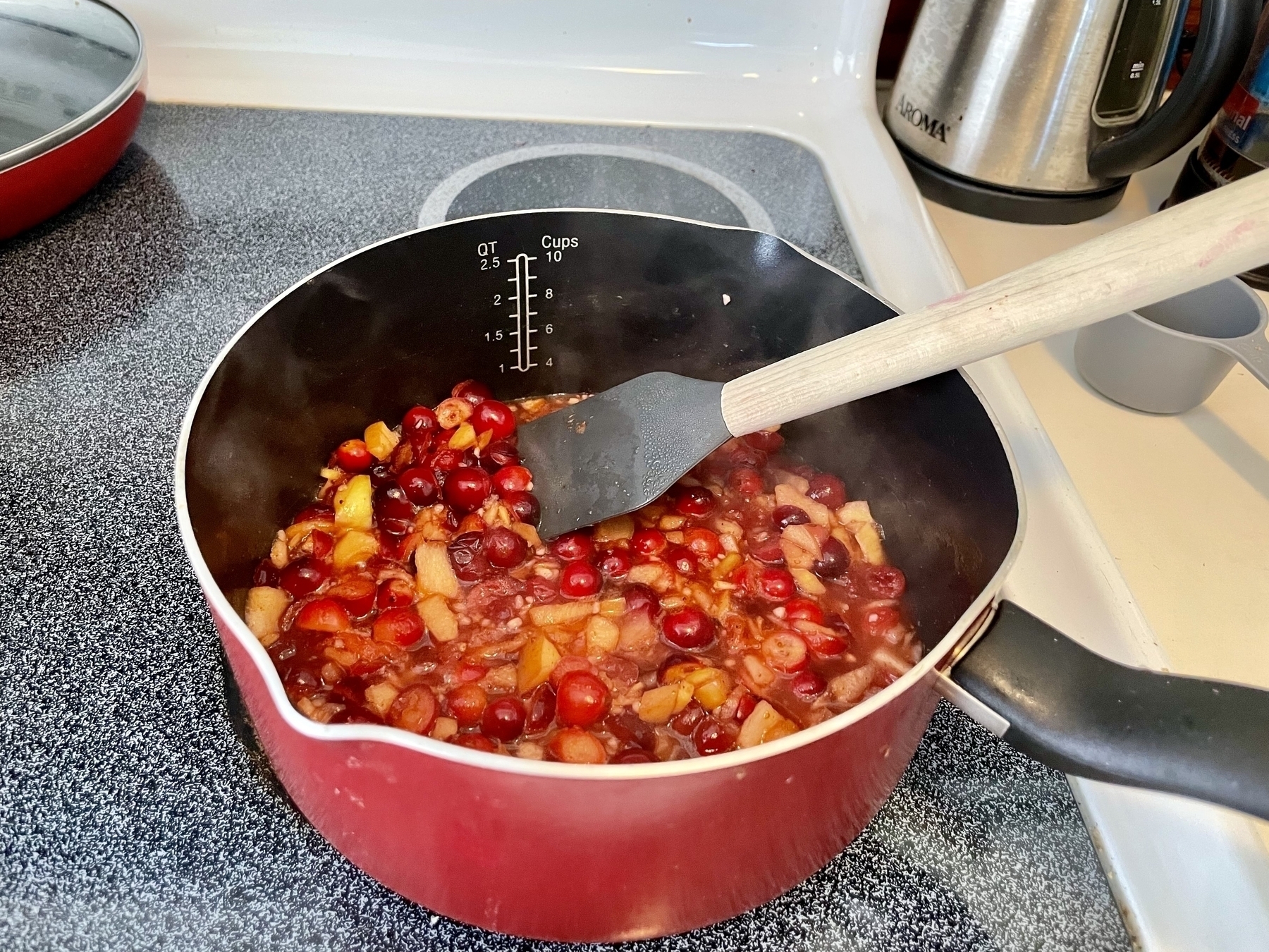 A pot on a stovetop filled with cranberries and chopped apple simmering in spices and apple cider vinegar 