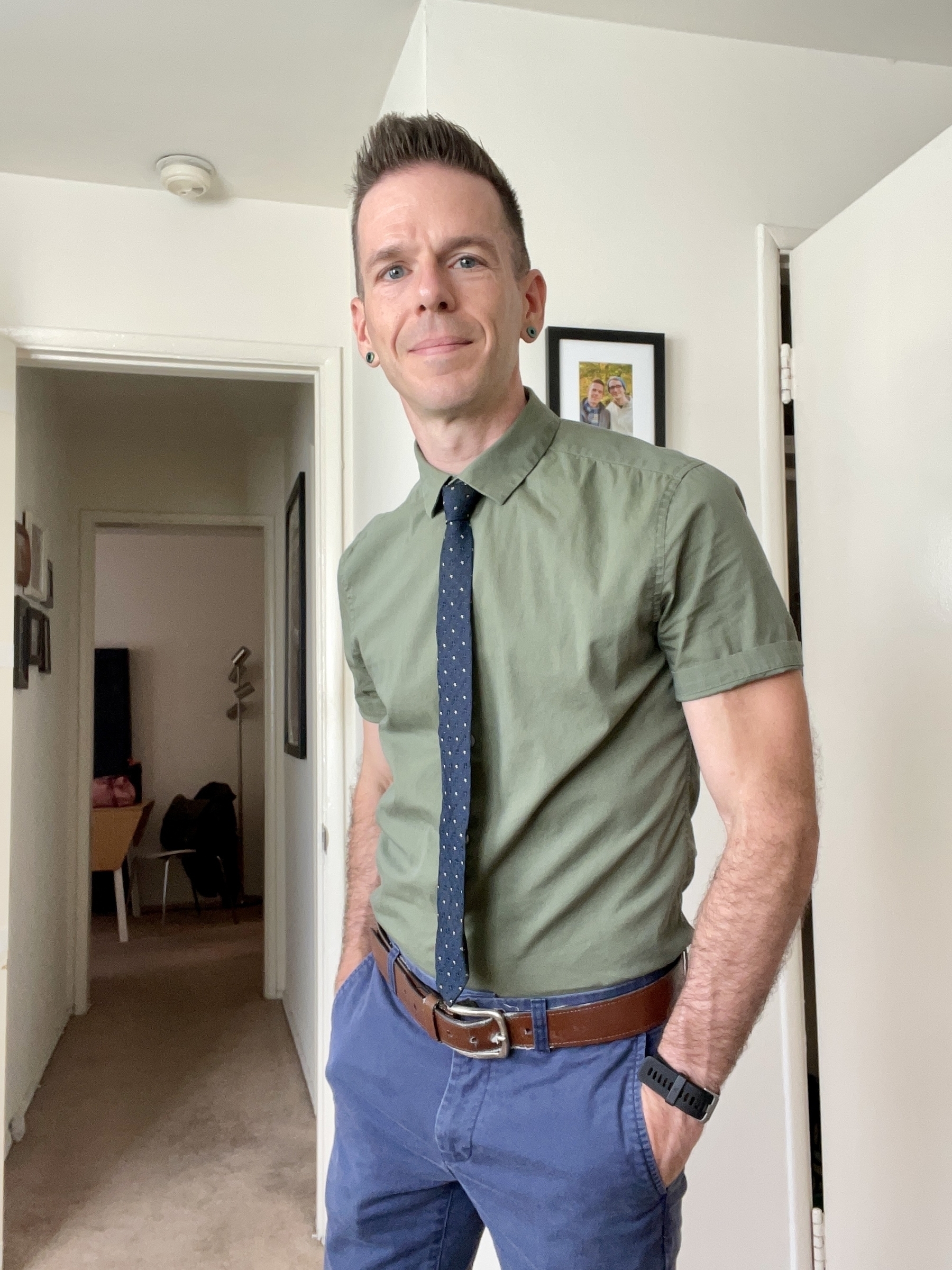 A man in a green short sleeved dress shirt with dark blue skinny necktie and blue slacks